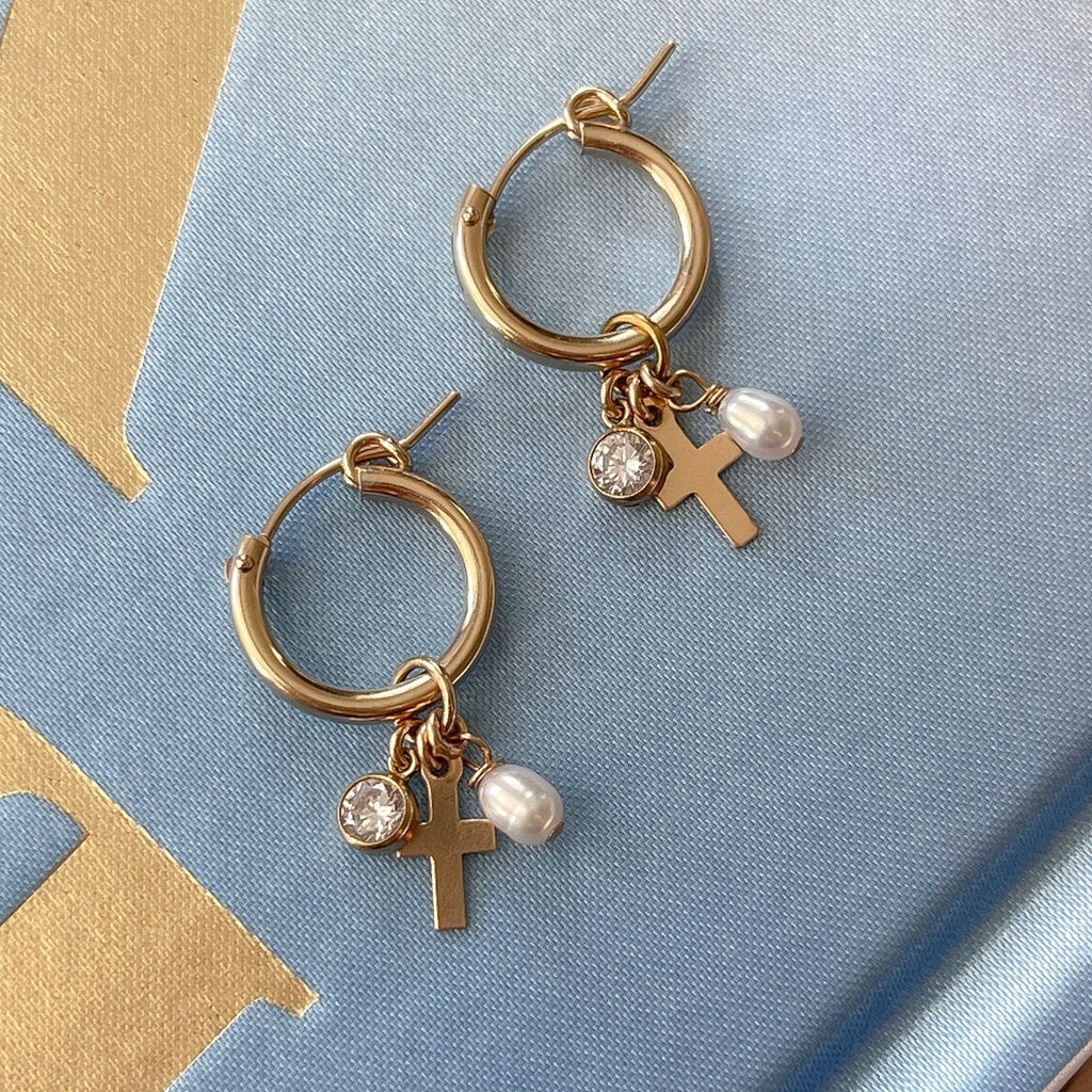 A pair of 15mm gold filled hoop earrings, each with three dangling charms — a sparkling CZ stone, a small white freshwater pearl, and a tiny gold cross — shown against a neutral background.